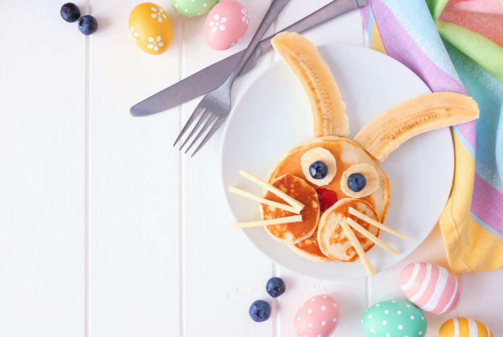 Cute Easter Bunny pancakes on a white plate. Corner border against a white wood background with copy space.