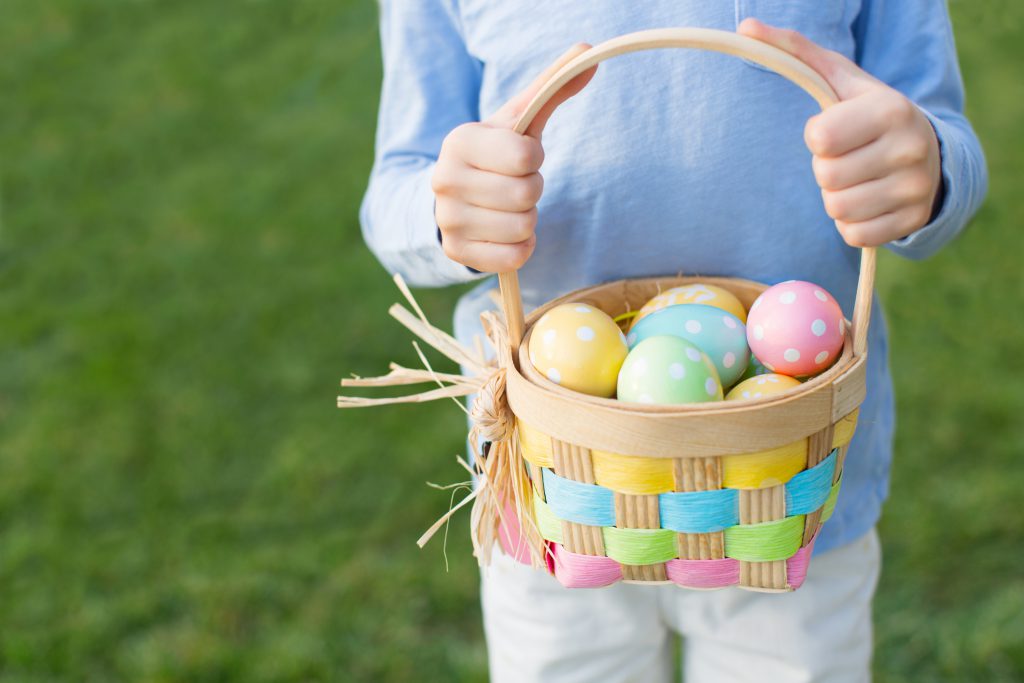 boy holding basket full of colorful easter eggs after egg hunt at spring time