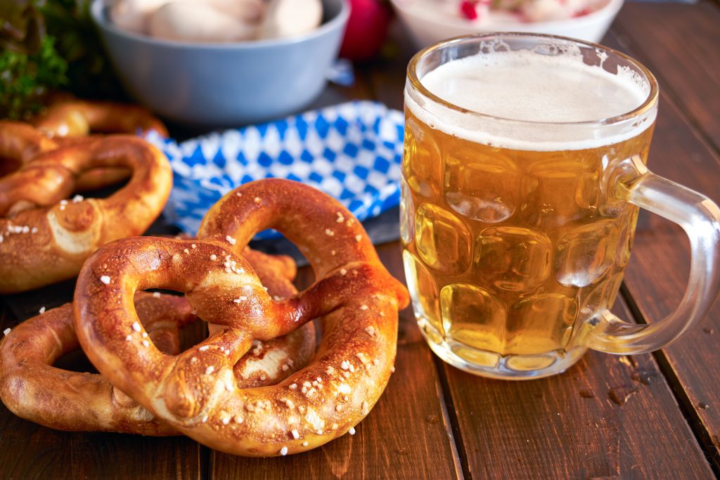 Traditional Munich pretzel next to mug of beer on wooden table for Beer Fest. Close up.